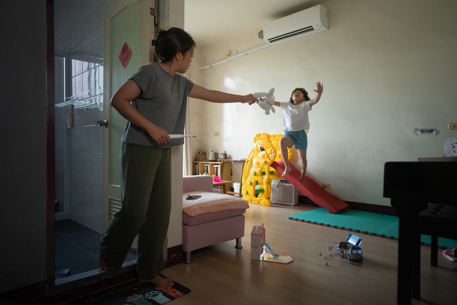 客廳裡母親遞出玩偶，孩子從溜滑梯上一躍而下伸手去接