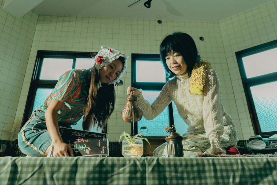 白磁磚老屋裡兩名女子俯身，其中一人手持銅壺沖水