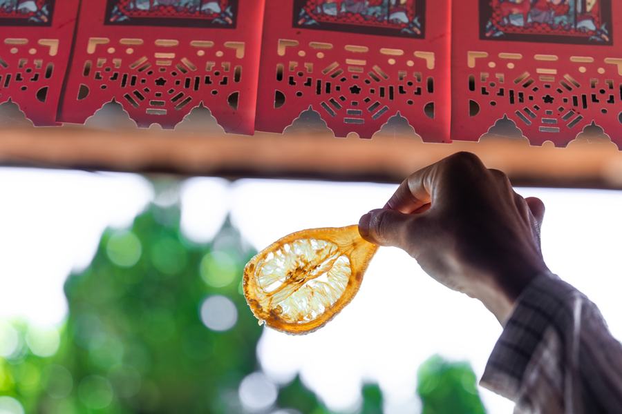 逆光下手持風乾柚片，背景是紅色剪紙窗花與綠意