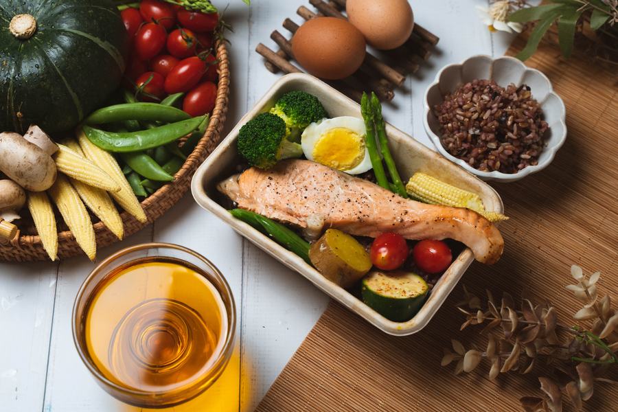 竹蓆上的烤鮭魚便當，旁邊擺著南瓜、玉米筍、甜豆與糙米飯