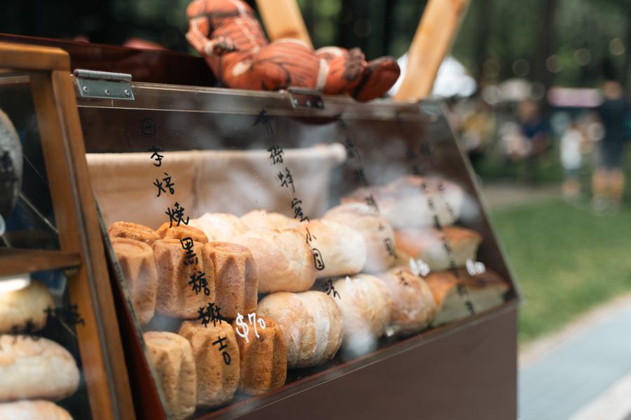 市集攤位玻璃櫃裡的麵包與甜點，標示著品名與價格