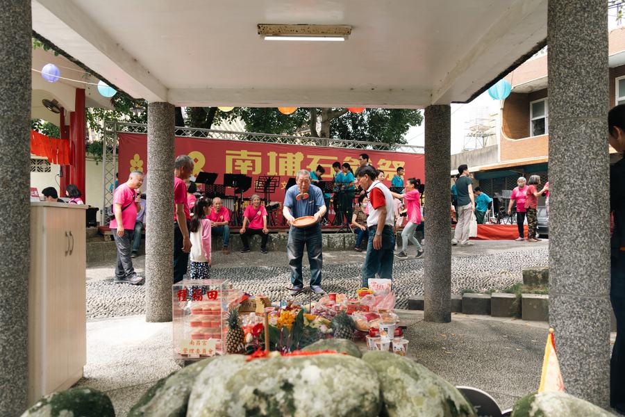 南埔石爺祭現場，長者在供桌前擲筊，樂隊在紅色布條下演奏